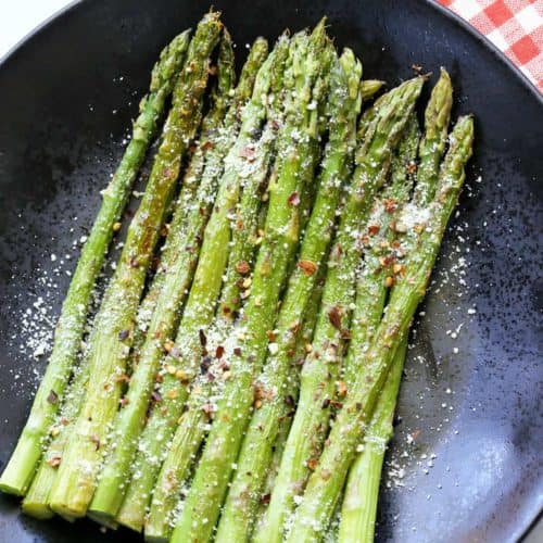 Roasted asparagus is topped with Parmesan and served on a dark plate.