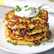 Yellow squash fritters are stacked on a white plate.