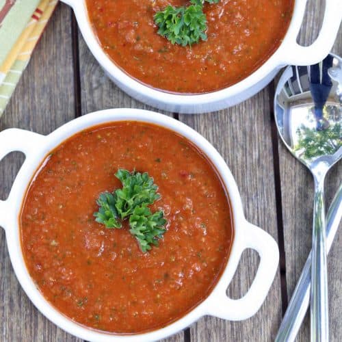 Gazpacho is served in white bowls with spoons.