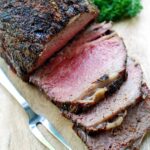 A sliced ribeye roast is served on a cutting board.