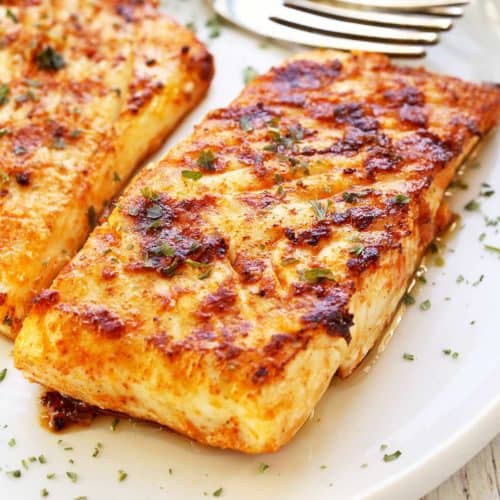 Grilled halibut is served on a white plate with a fork.
