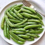 Sauteed sugar snap peas are served on a white plate with a fork.