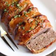 Bacon-wrapped meatloaf, sliced, is served on a white plate.
