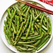 Chinese green beans are served on a white plate with chopsticks.
