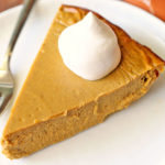 Keto pumpkin pie is topped with a dollop of whipped cream.
