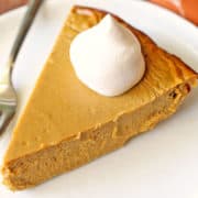 Keto pumpkin pie is topped with a dollop of whipped cream.