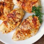Broiled chicken is served on a white plate with a garnish of parsley.