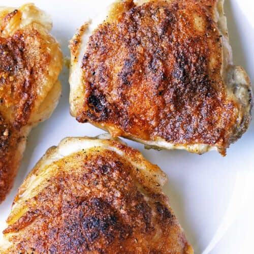 Crispy baked chicken thighs are served on a white plate.