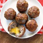 Cheese stuffed meatballs are served on a white plate with a napkin.