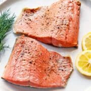 Poached salmon is served on a white plate with lemon slices.