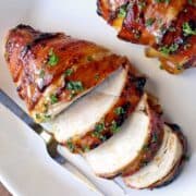 Bacon wrapped chicken breast is served on a white plate.
