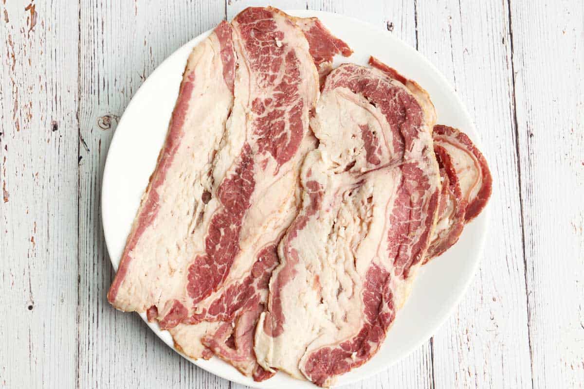 Raw beef bacon slices arranged on a white plate. 
