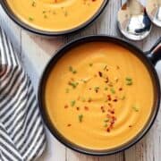 Butternut squash soup is served in a dark bowl.