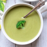 Cream of broccoli soup is served in a white bowl with a spoon.