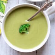 Cream of broccoli soup is served in a white bowl with a spoon.
