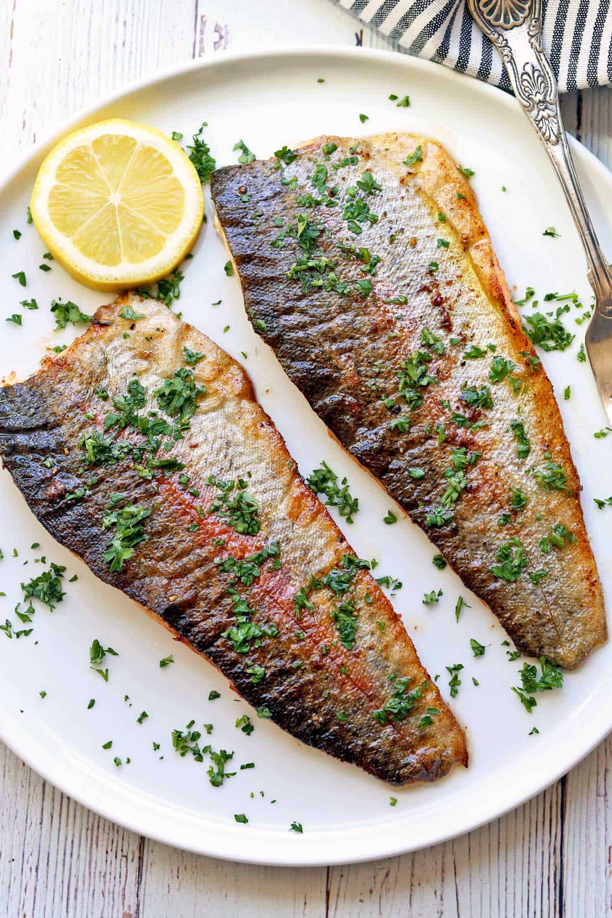 Two rainbow trout fillets are served on a white plate. 