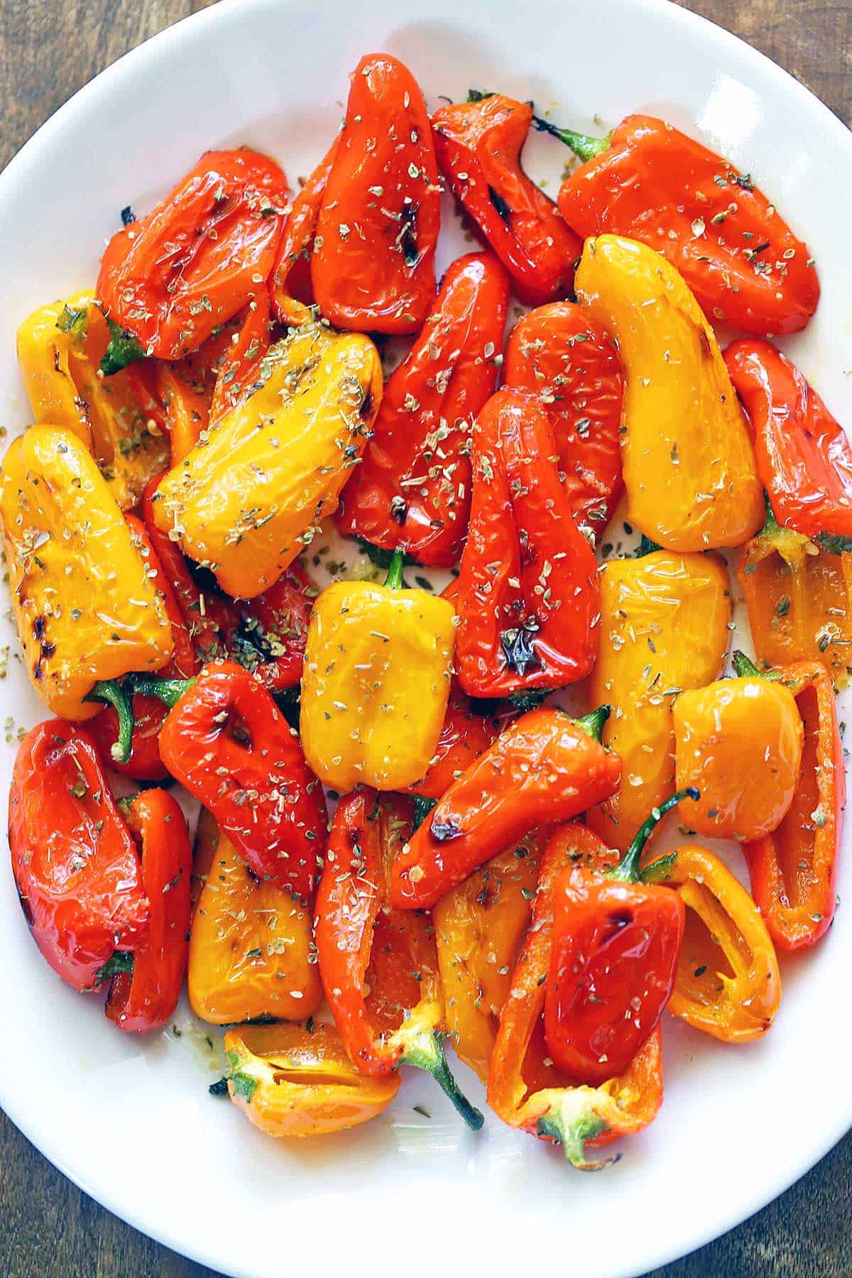 Roasted mini peppers are served on a white platter. 