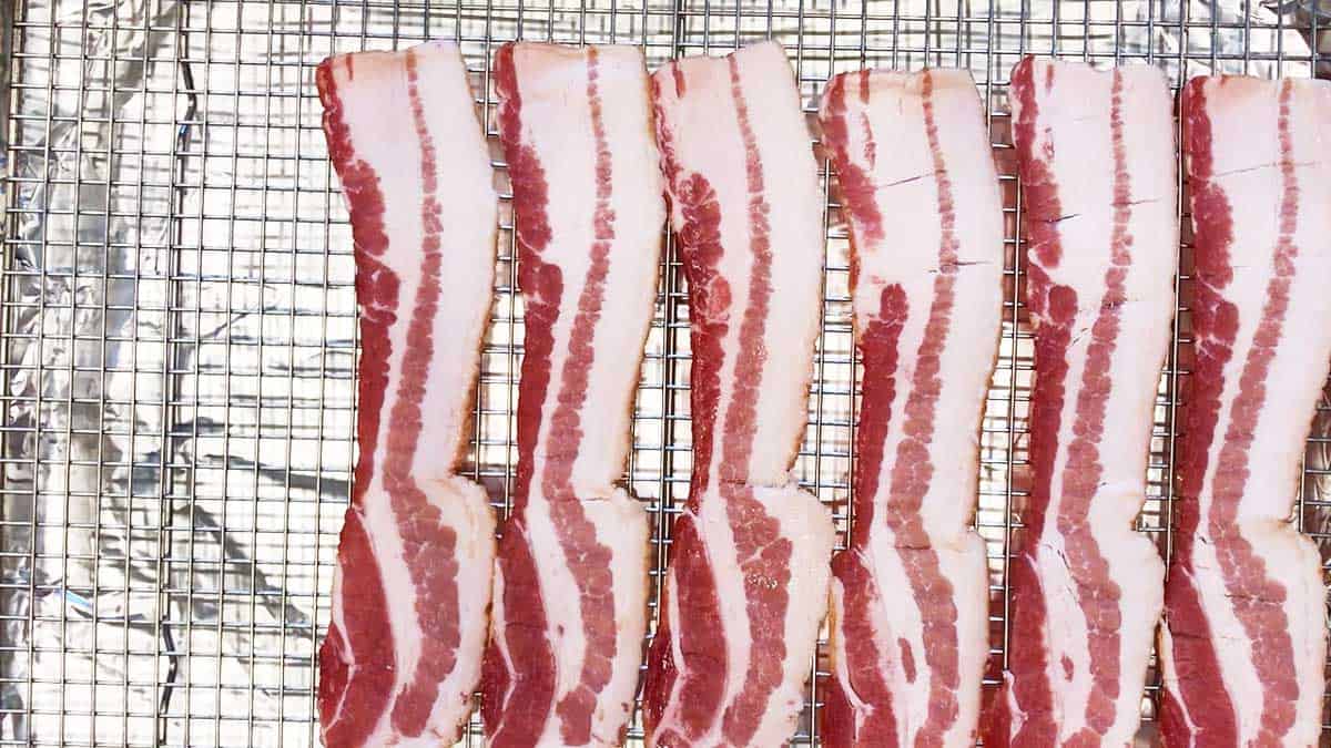 Raw bacon strips arranged on a wire rack. 