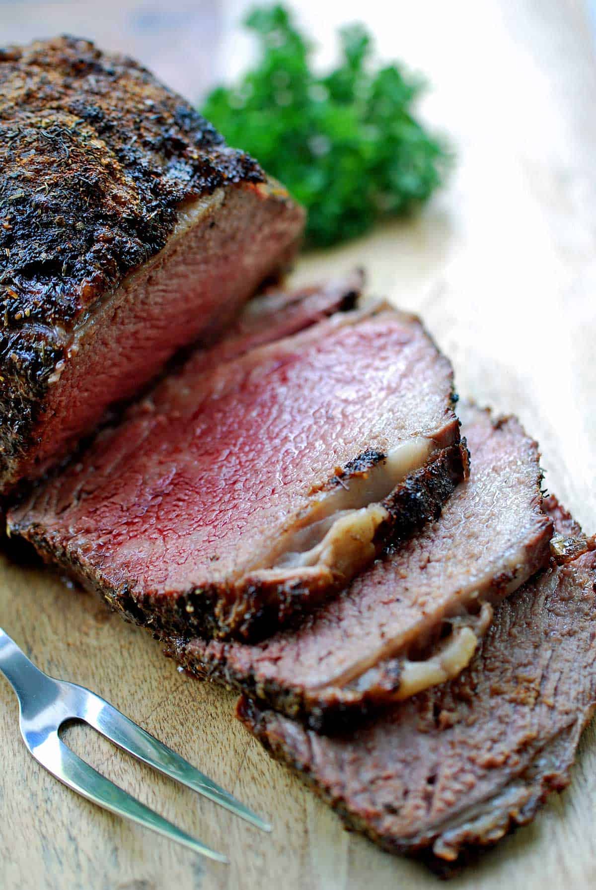A ribeye roast is served on a wooden cutting board with a garnish of parsley.
