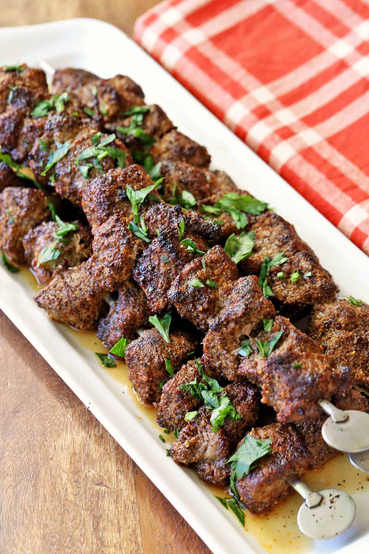 Beef kabobs served on a white tray with a red napkin.