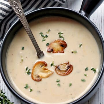 Cream of mushroom soup is served in a dark bowl with a spoon.