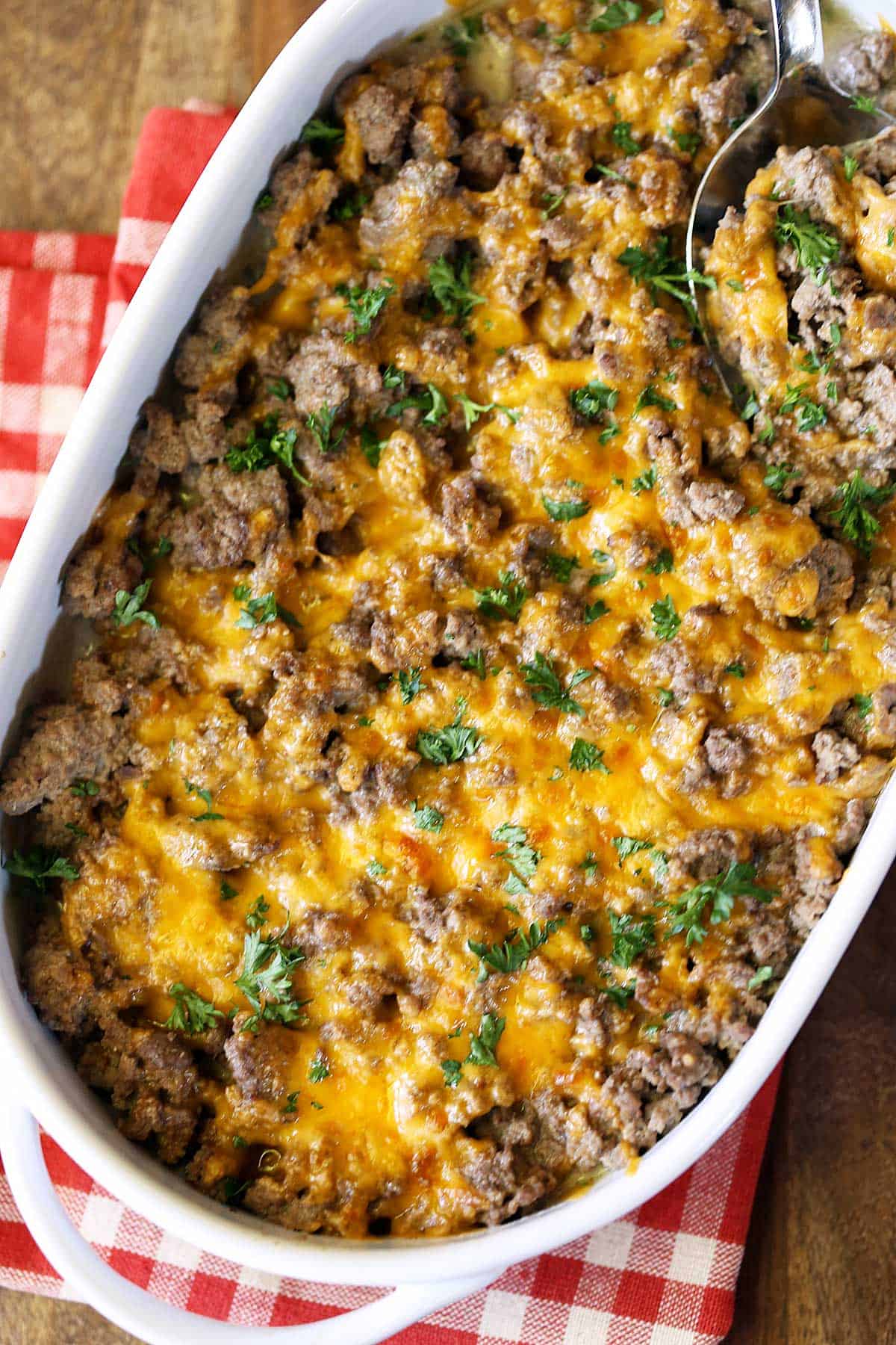 Ground beef casserole served in a white dish with a spoon and a red napkin. 