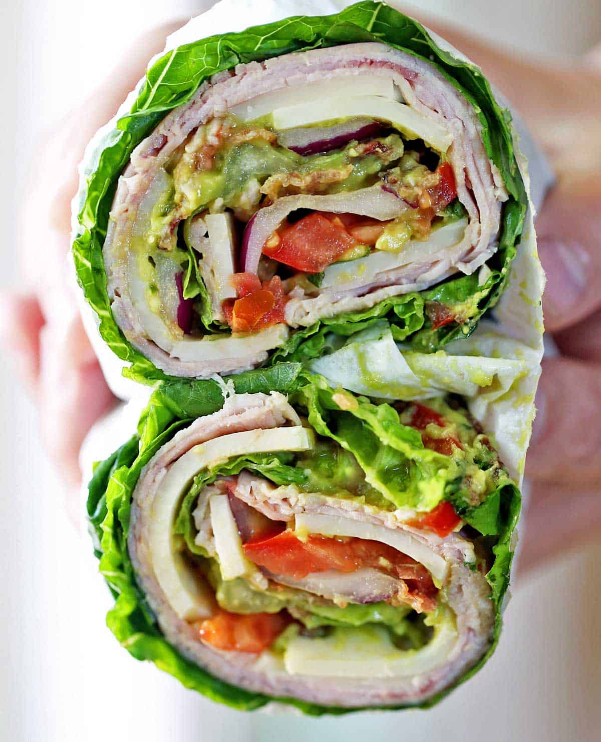 Hands are holding a lettuce sandwich.