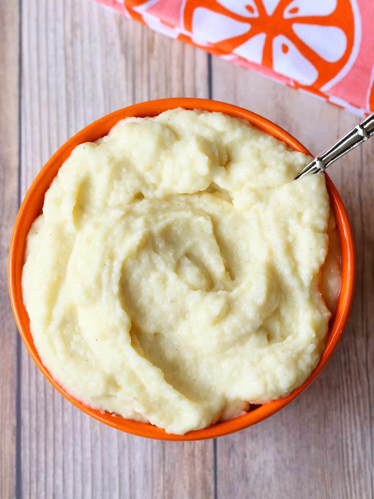 Mashed cauliflower is served in a bowl with a spoon. 