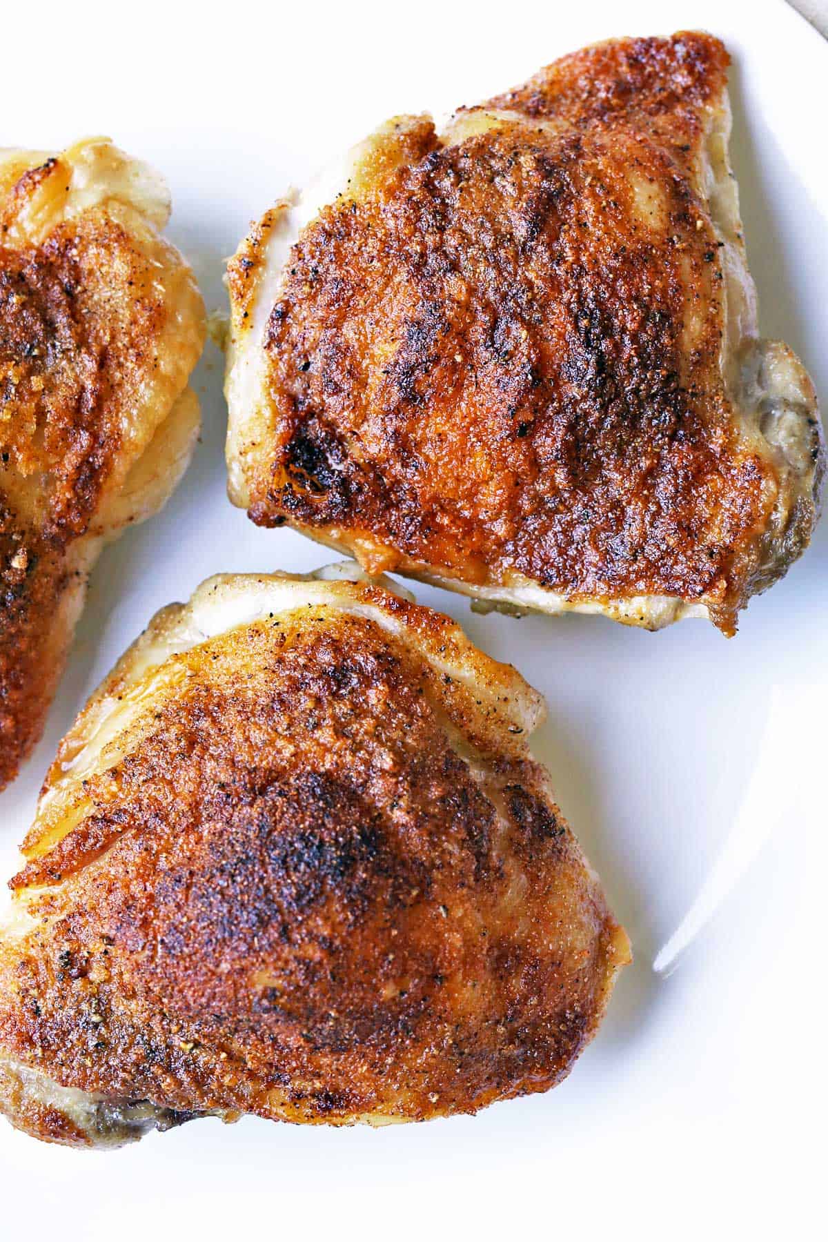 Three crispy-skinned baked chicken thighs on a plate.