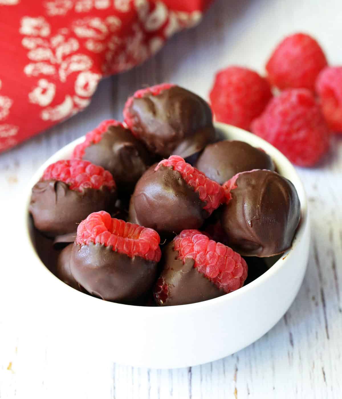 Chocolate covered raspberries are served in a white bowl. 