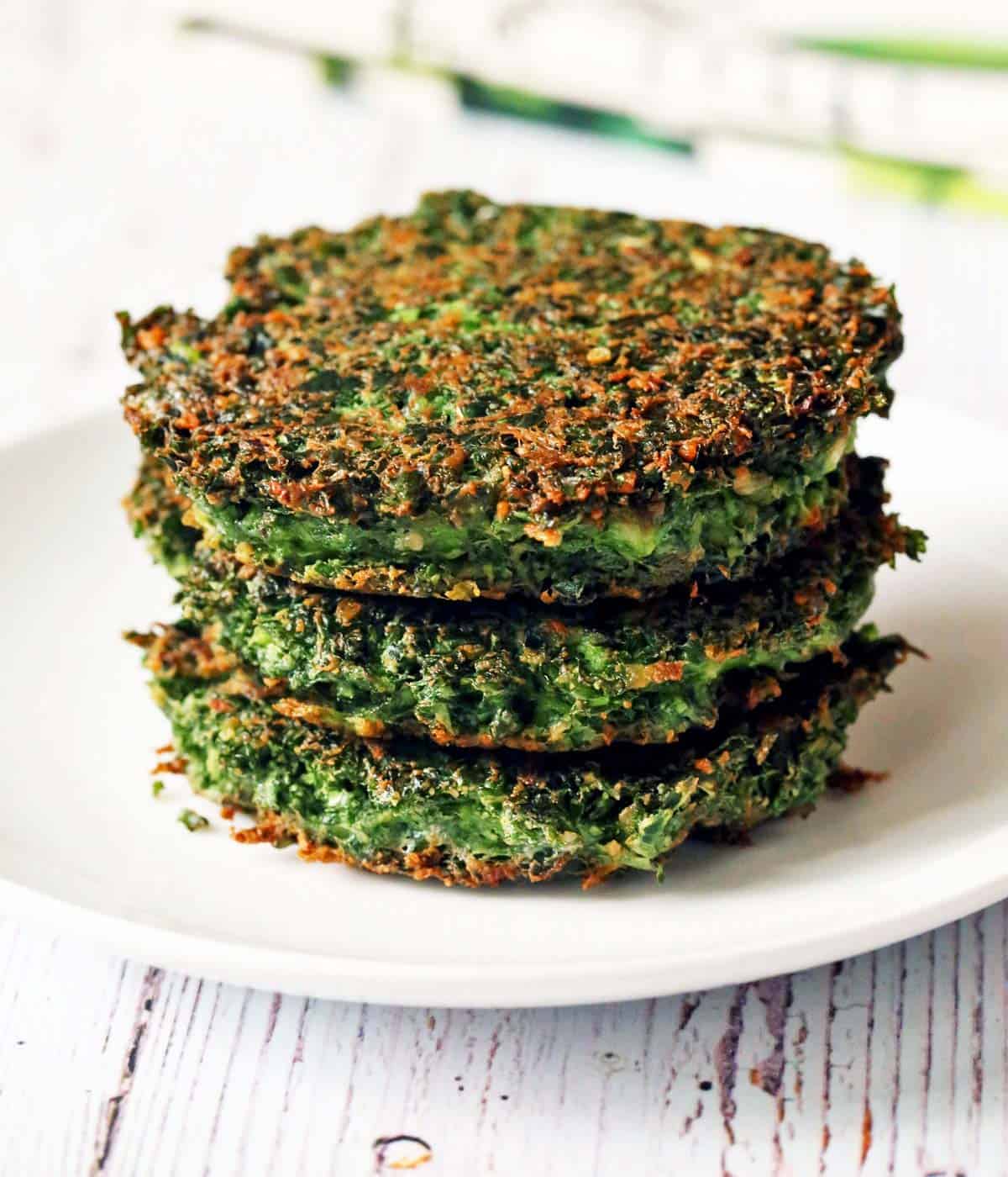 Three kale fritters are stacked on a white plate. 