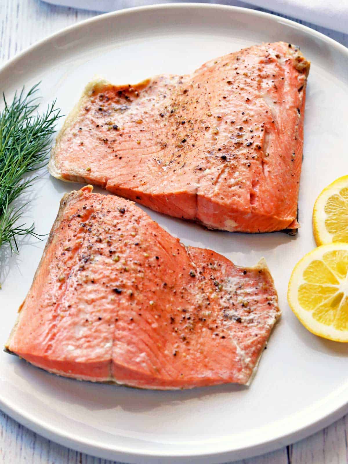 Two poached salmon fillets are served with lemon slices and dill. 