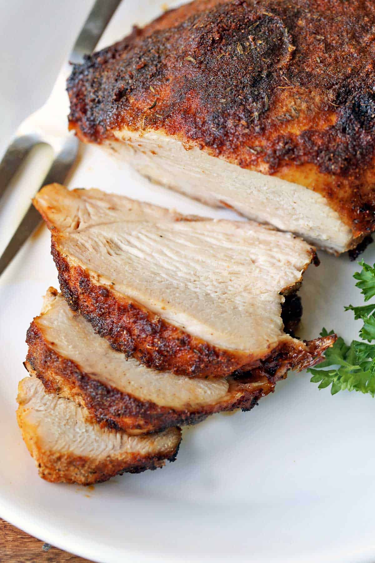 Sliced boneless turkey breast is served on a plate and garnished with parsley. 