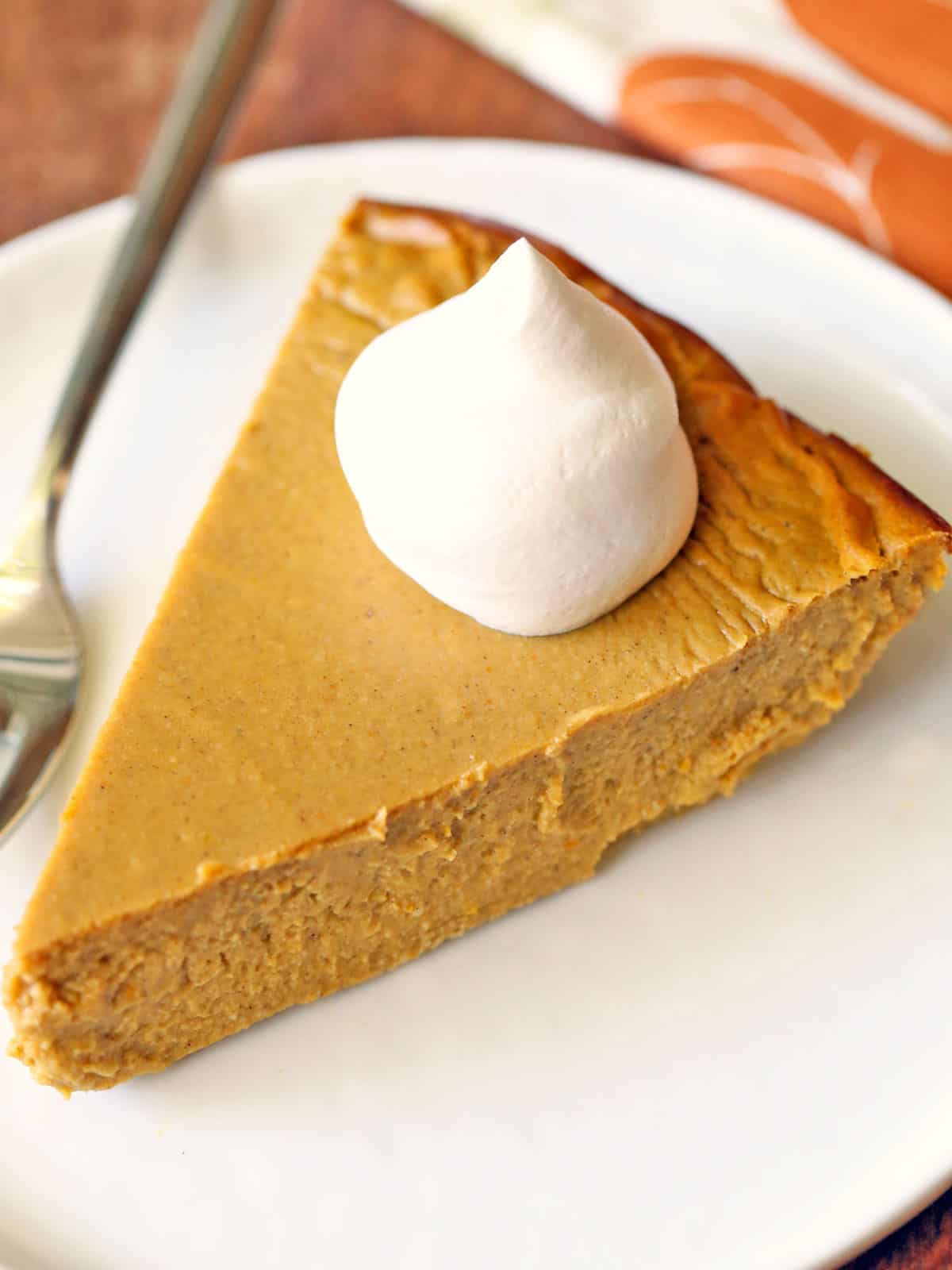 A slice of keto pumpkin pie is topped with whipped cream.