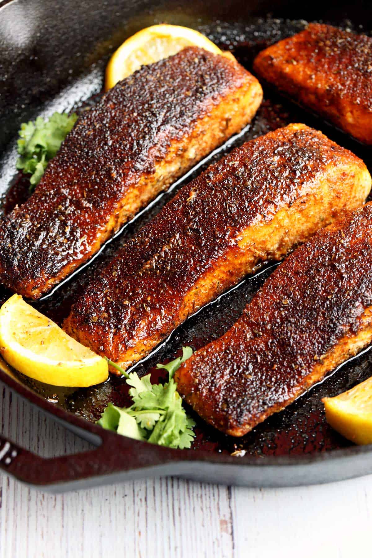 Blackened salmon is served in a cast-iron skillet with lemon slices. 