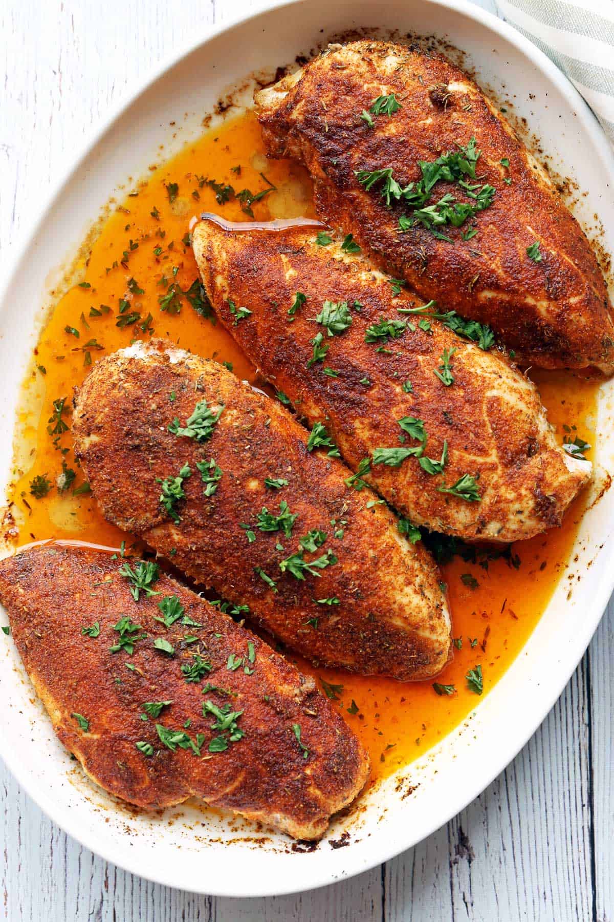 Four Cajun chicken breasts are served in a white baking dish, topped with parsley. 
