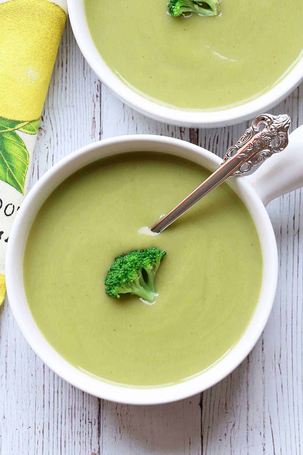 Cream of broccoli soup is served in white bowls. 