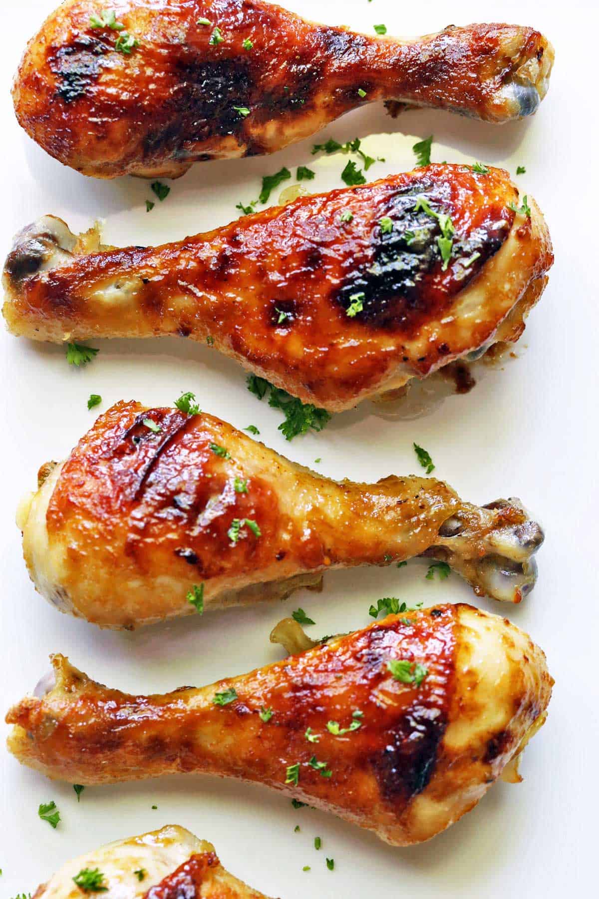 Honey garlic chicken drumsticks are served on a white plate.