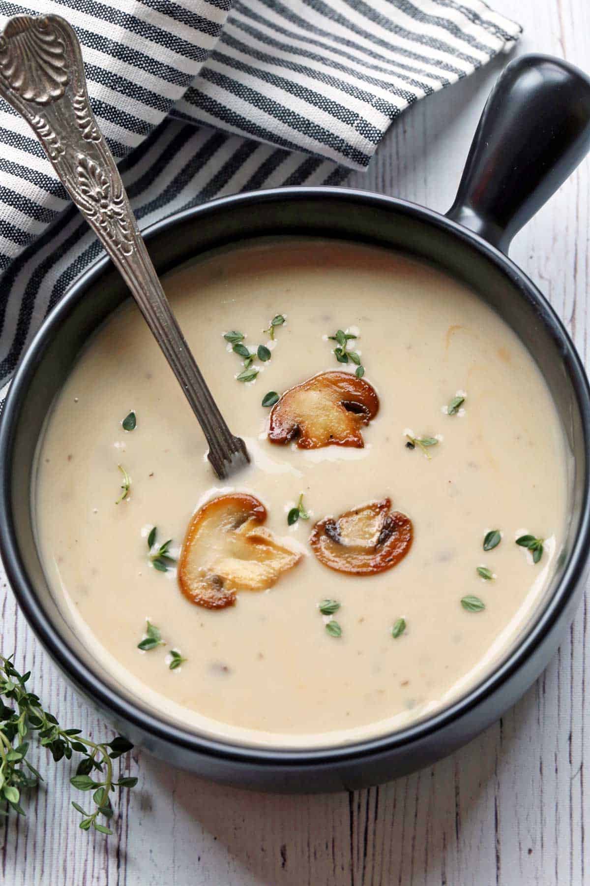 Cream of mushroom soup is served in a black soup bowl and garnished with mushrooms.  