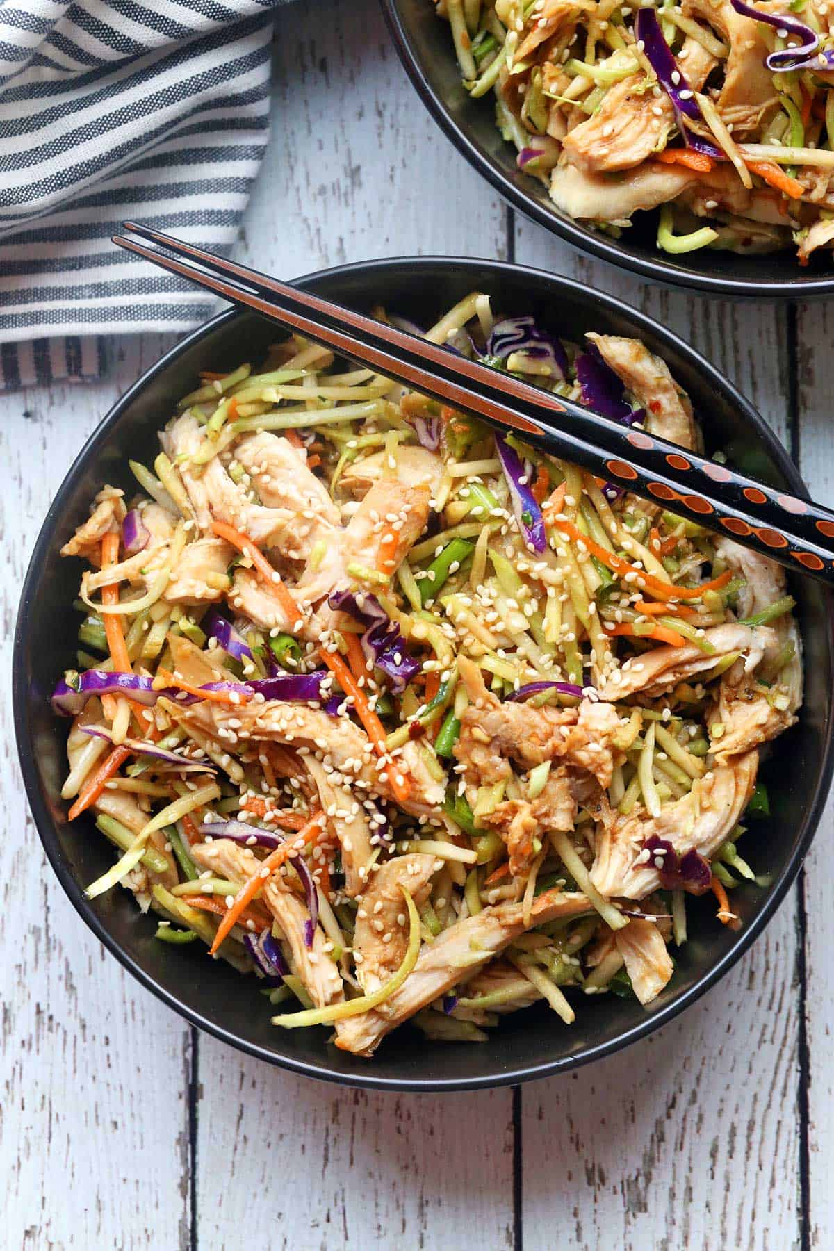 Chinese chicken salad is served in a black bowl with chopsticks. 