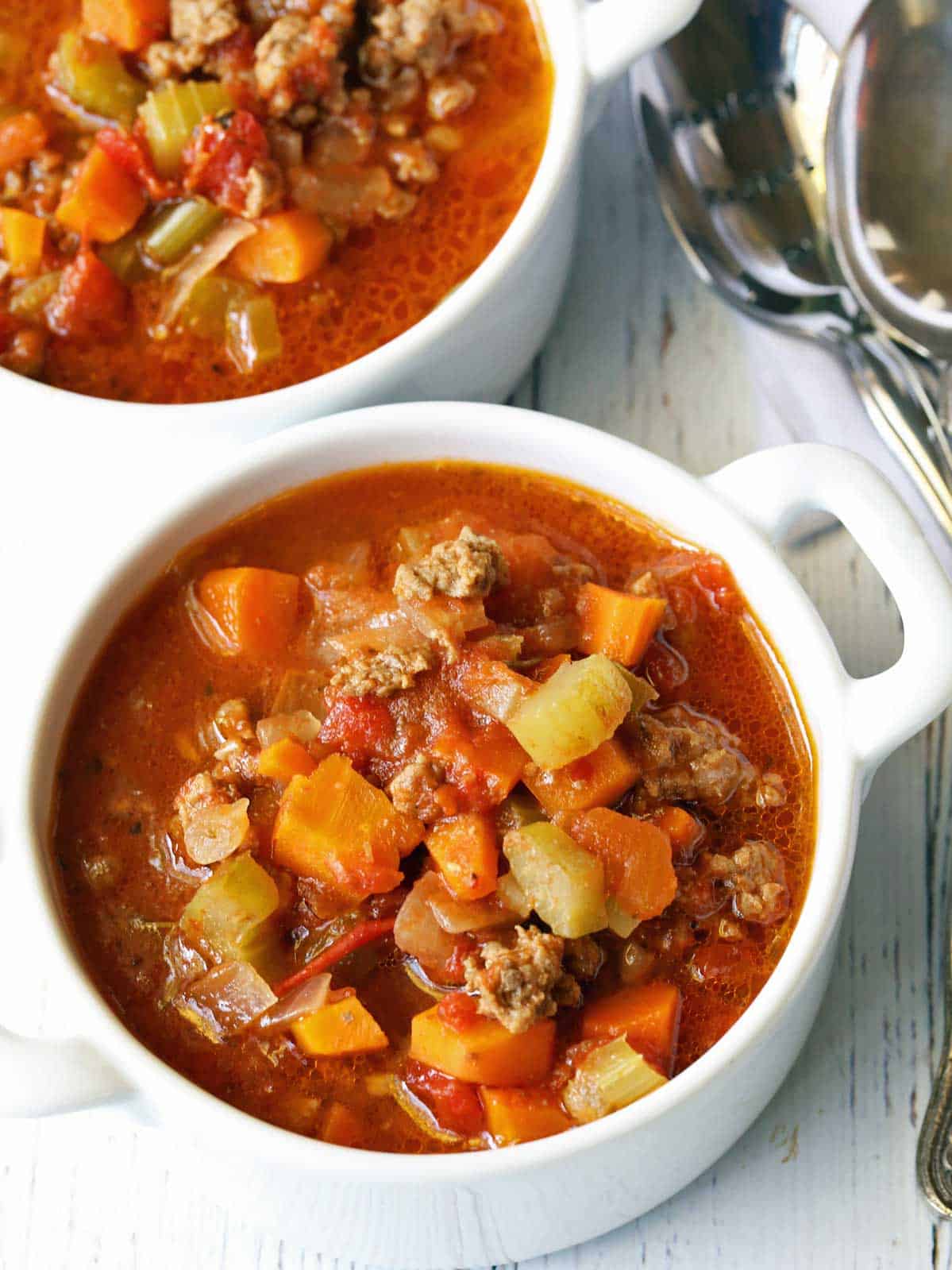 Vegetable beef soup is served in two white bowls. 