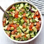 Israeli salad is served in a white bowl with a serving spoon.