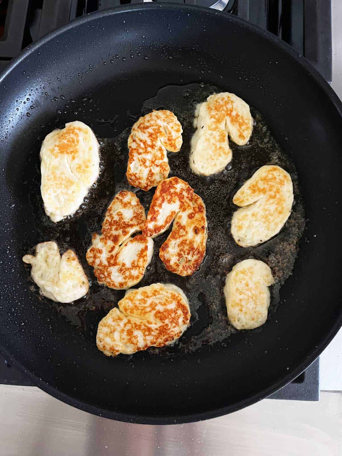 Halloumi slices getting pan-fried in a skillet. 