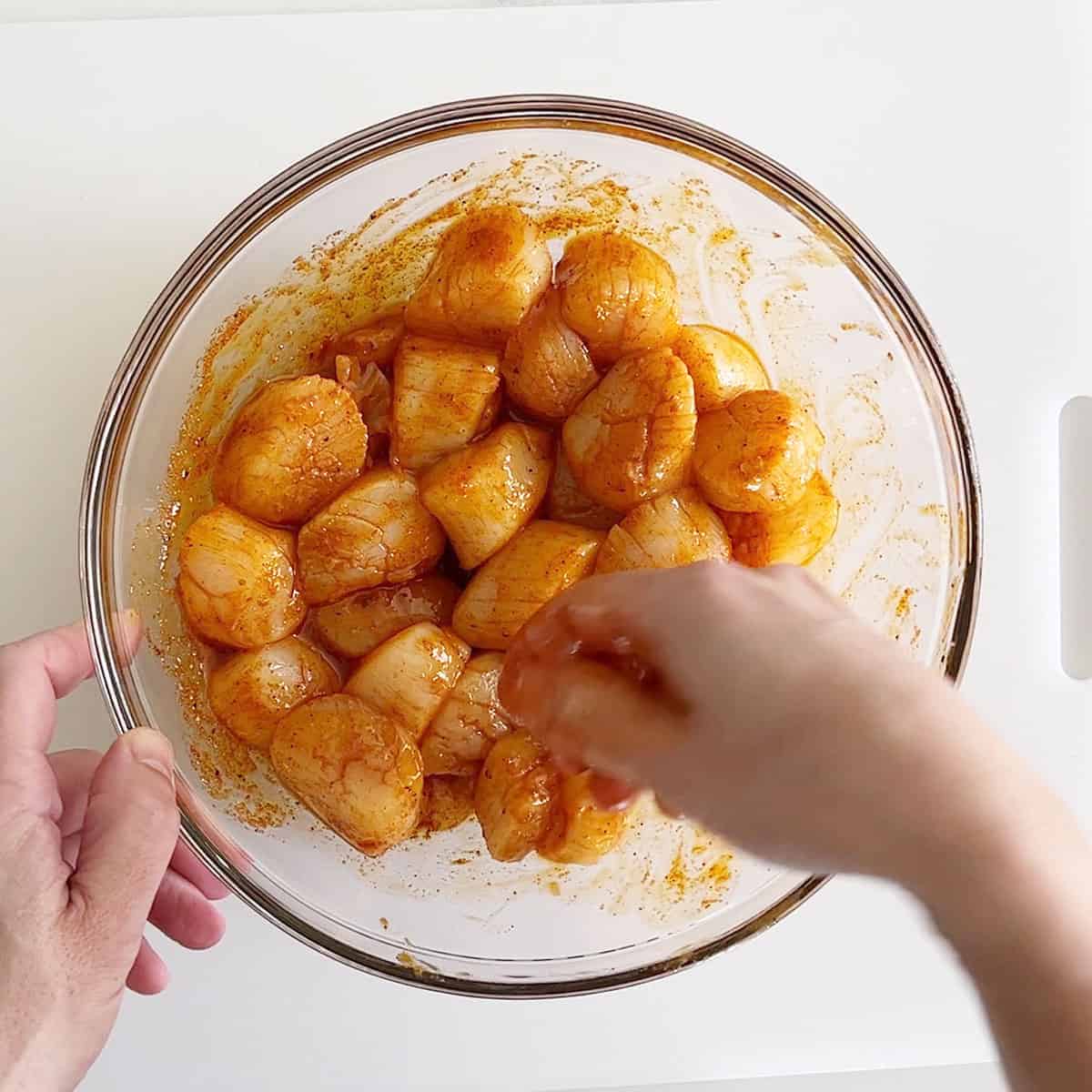 Coating the scallops in oil and spices. 