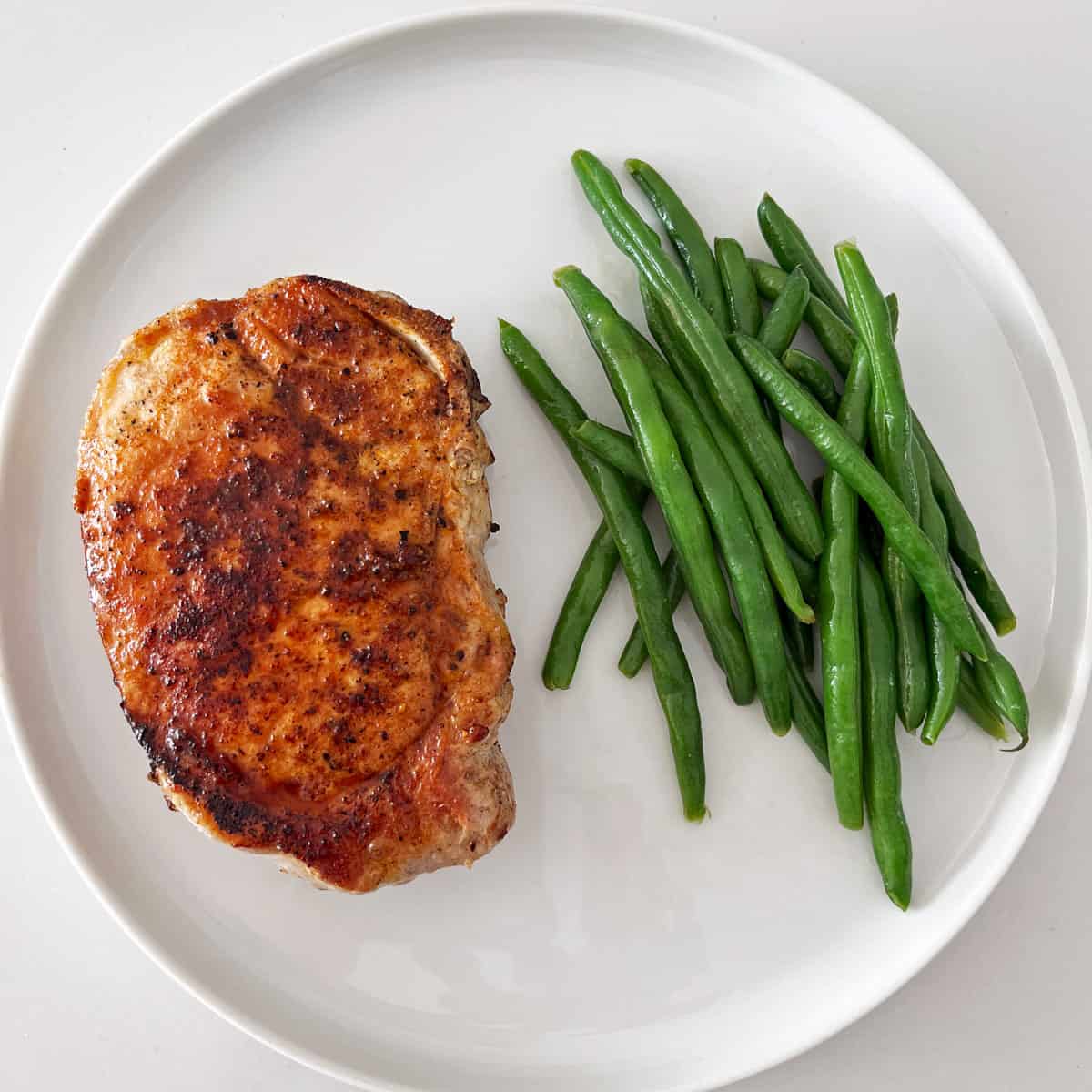 A baked pork chop is served with green beans.