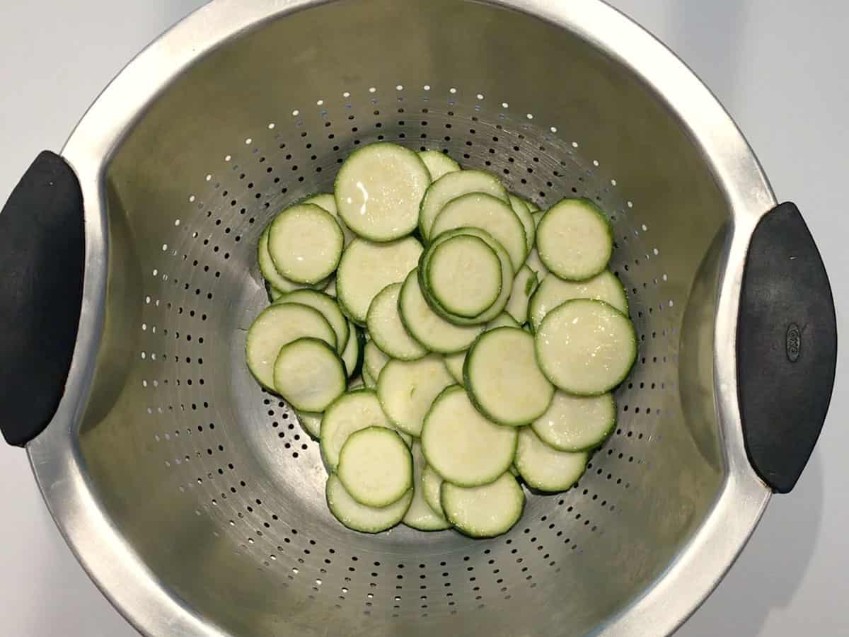 Salting the zucchini slices. Water drops are visible on the zucchini surface. 