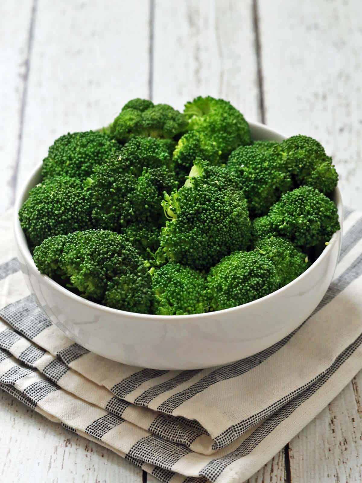 Steamed broccoli is served in a white bowl with a napkin.