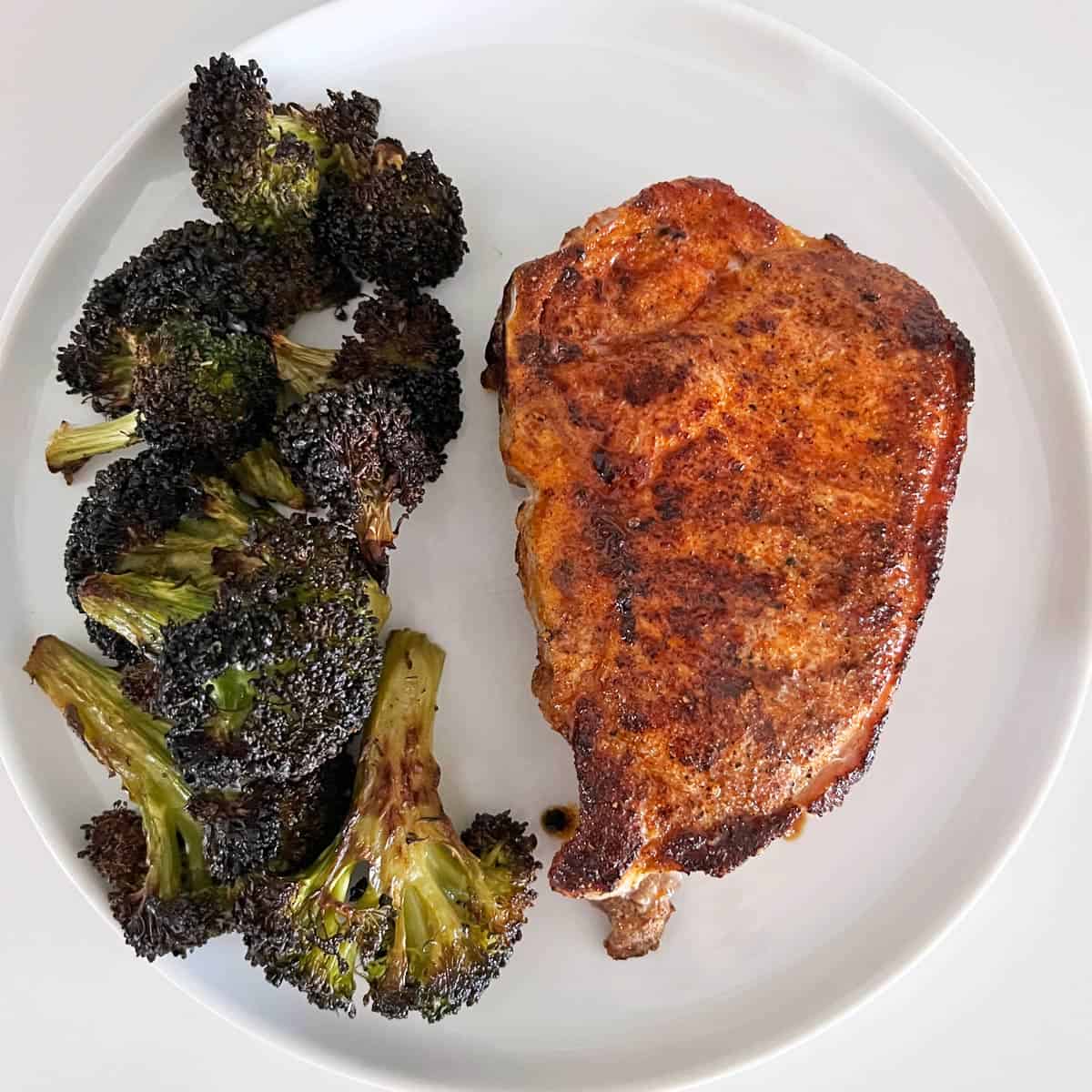 A baked pork chop is served with roasted broccoli.