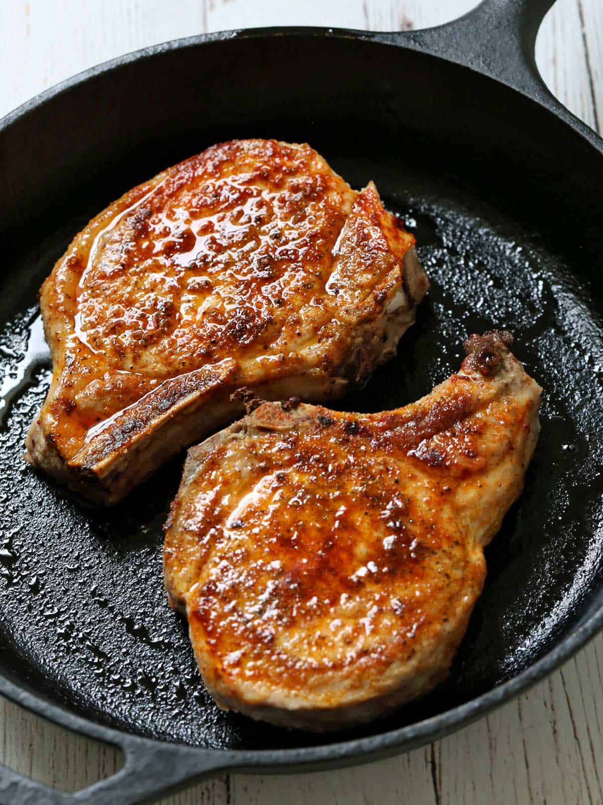 Two baked pork chops in a cast-iron skillet.