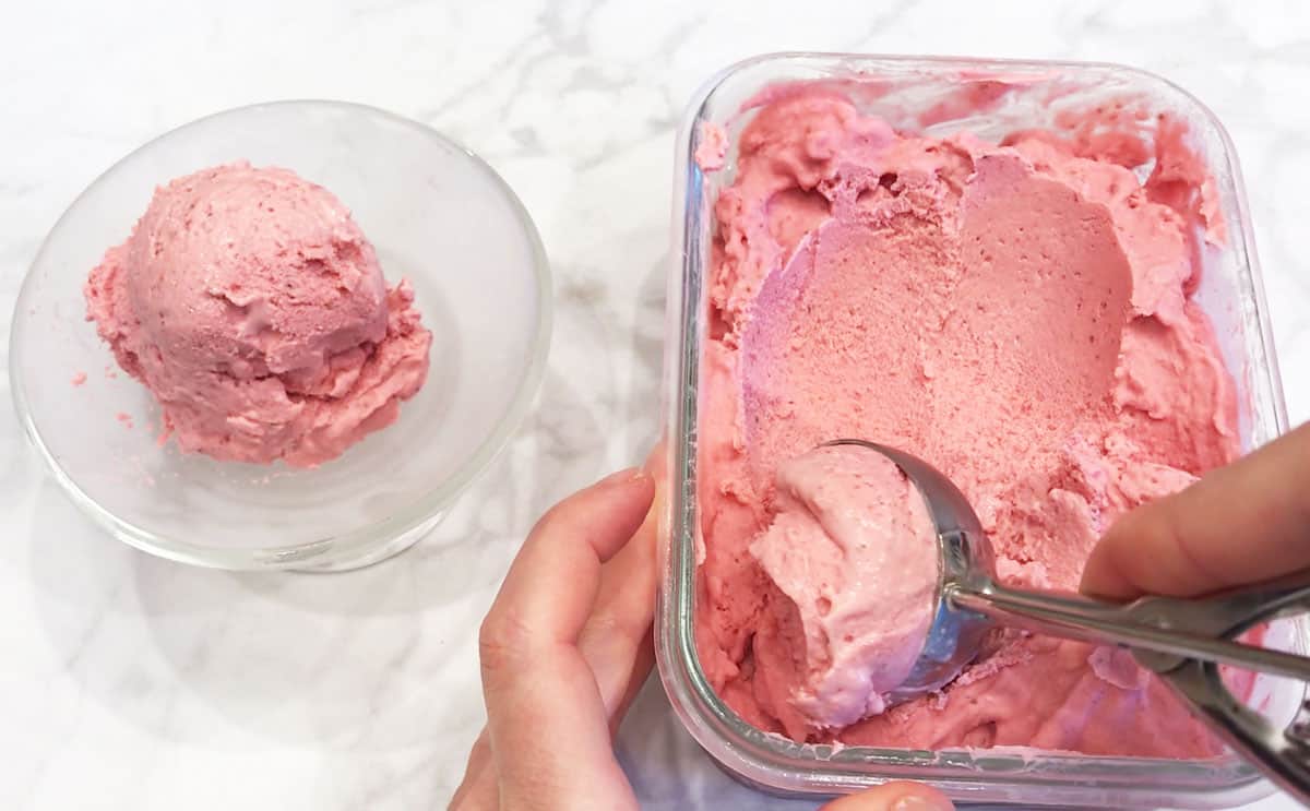 Scooping the ice cream into a glass dessert bowl.